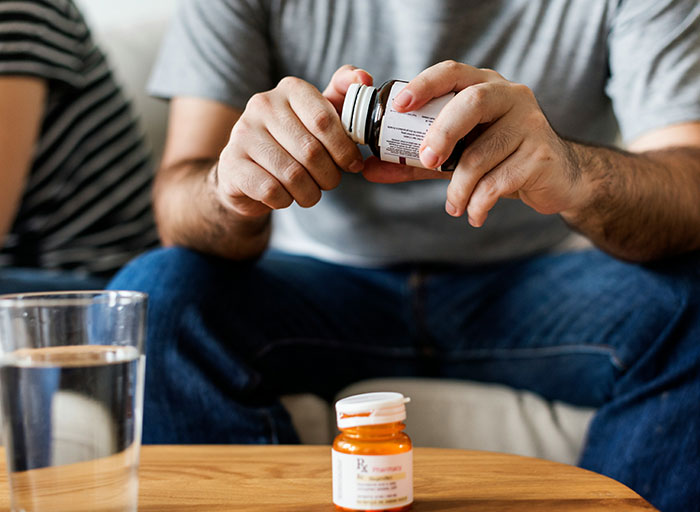 Close-up of a person holding a pill bottle with medication on a table, illustrating psychologists and patients concepts.