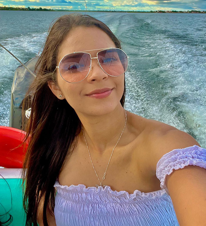 Young beauty queen wearing sunglasses and a purple top taking a selfie on a boat in a scenic water setting.