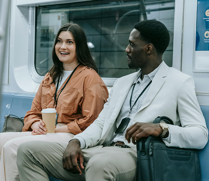 Two colleagues talking on a subway, one smiling and holding a coffee, representing job referral and bonus discussion.