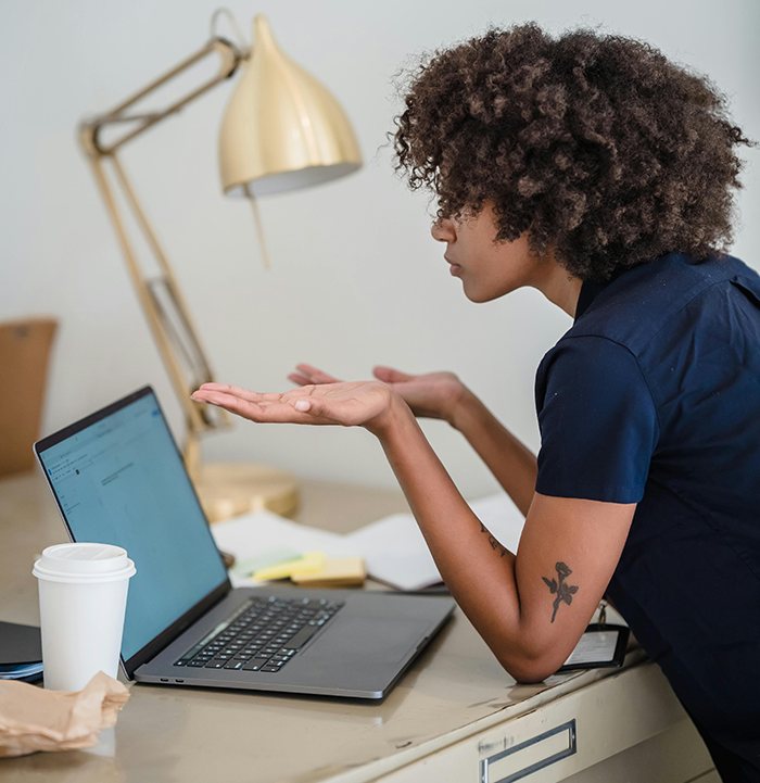 Person with curly hair gesturing at laptop screen in home office, discussing job referral and referral bonus.