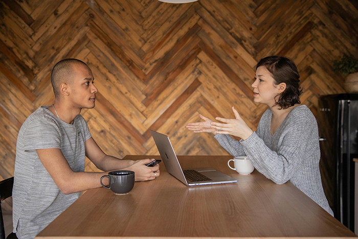 Two colleagues discussing a referral bonus and job opportunity over coffee with a laptop between them.