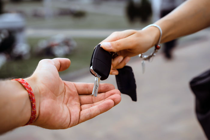 A person handing over car keys to another, symbolizing a jobless guy expecting a provider girlfriend to share her win.
