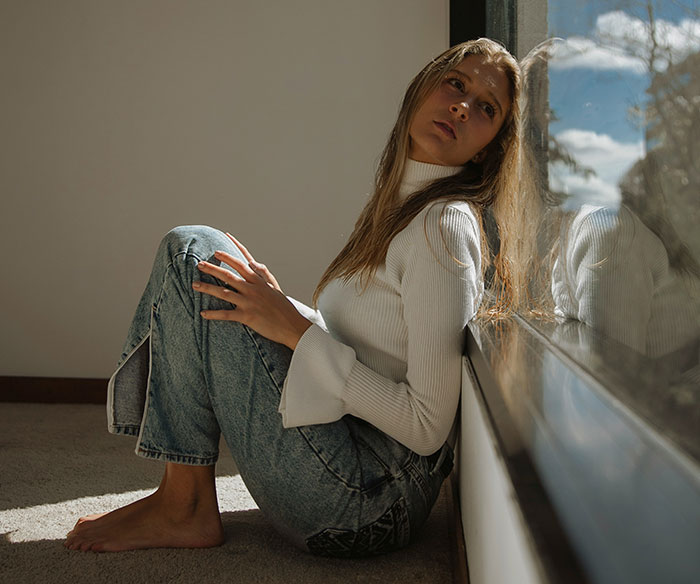 Young woman with long hair sitting by a window, reflecting on refusing to cut her hair for boyfriend&rsquo;s mom party.