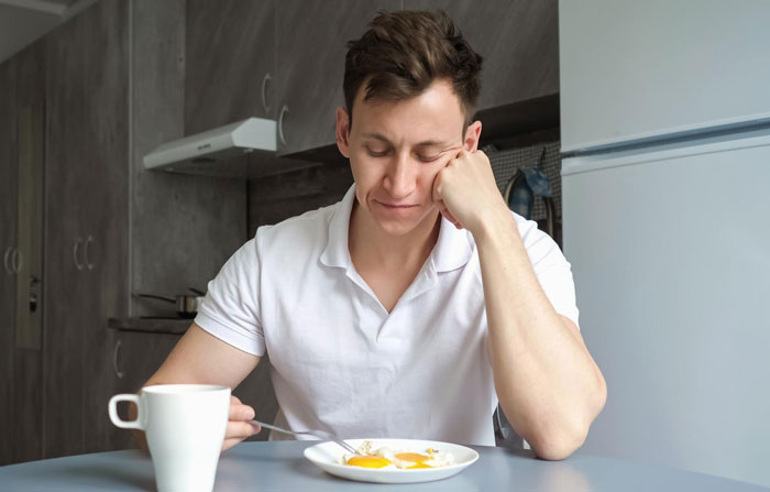 Young man refusing to eat vegan meal looking disappointed at breakfast on girlfriend's birthday in a modern kitchen. Young man refusing to eat vegan meal looking disappointed at breakfast on girlfriend's birthday in a modern kitchen.