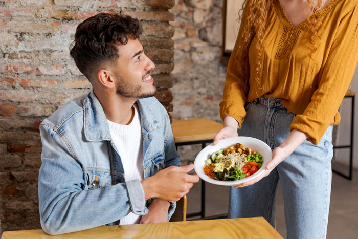 Man hesitating to eat vegan meal offered by girlfriend during birthday celebration at cozy restaurant table. Man hesitating to eat vegan meal offered by girlfriend during birthday celebration at cozy restaurant table.
