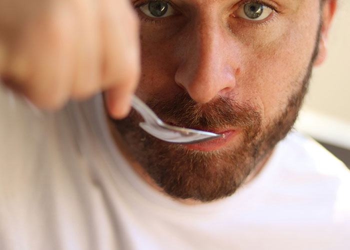 Close-up of a man tasting food with a spoon, illustrating a roommate conflict over sharing homemade meals. Close-up of a man tasting food with a spoon, illustrating a roommate conflict over sharing homemade meals.