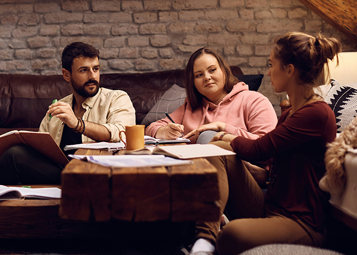 Three roommates having a serious discussion in a cozy living room about sharing homemade meals and being called stingy. Three roommates having a serious discussion in a cozy living room about sharing homemade meals and being called stingy.
