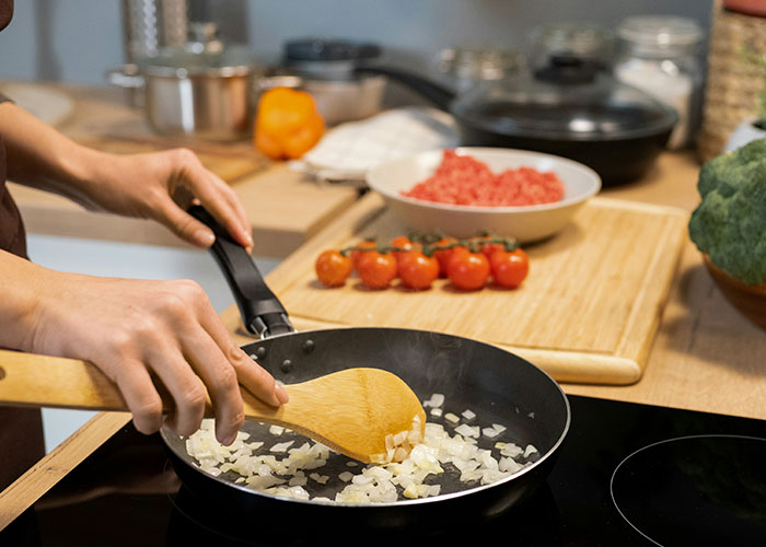 Person cooking onions in a frying pan, illustrating homemade meals related to roommate calls woman stingy sharing issue. Person cooking onions in a frying pan, illustrating homemade meals related to roommate calls woman stingy sharing issue.