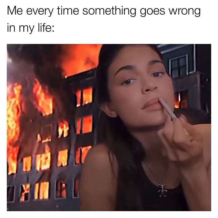 Woman showing middle finger with calm expression in front of burning building, capturing chaos of navigating the world today.