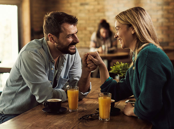 Couple smiling and fist bumping at a cafe, highlighting woman learning boyfriend stalked her before they met. Couple smiling and fist bumping at a cafe, highlighting woman learning boyfriend stalked her before they met.