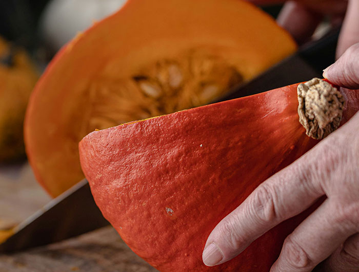 Hand cutting a pumpkin slice on a wooden board, symbolizing fresh ingredients in chain restaurant employee warnings.