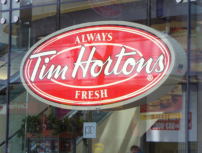 Tim Hortons chain restaurant sign with red oval logo, reflecting glass storefront and interior decor.