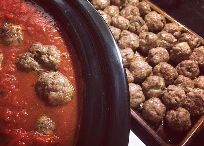 Cooked meatballs in tomato sauce in a pot next to a baking tray filled with browned meatballs, chain restaurant advice.