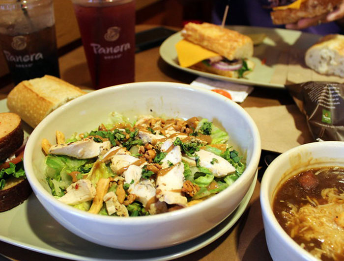 Salad and soup meal at a chain restaurant with drinks and sandwich pieces on a table setting