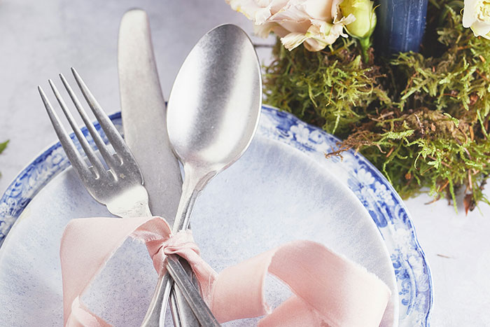 Silver fork, knife, and spoon tied with pink ribbon on a blue and white plate, symbolizing rich people behavior.