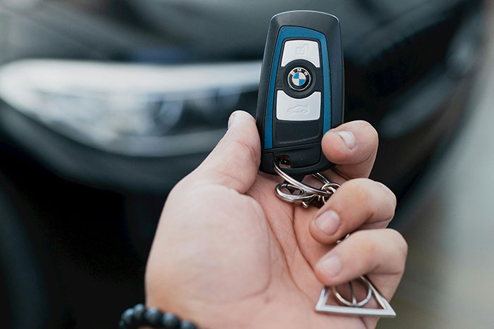 Close-up of a hand holding a BMW car key, illustrating rich people behavior and luxury lifestyle details.