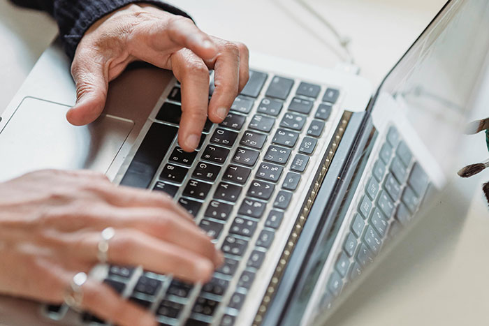 Hands typing on a laptop keyboard, illustrating rich people behavior shared by staff from high-end hotels and restaurants.