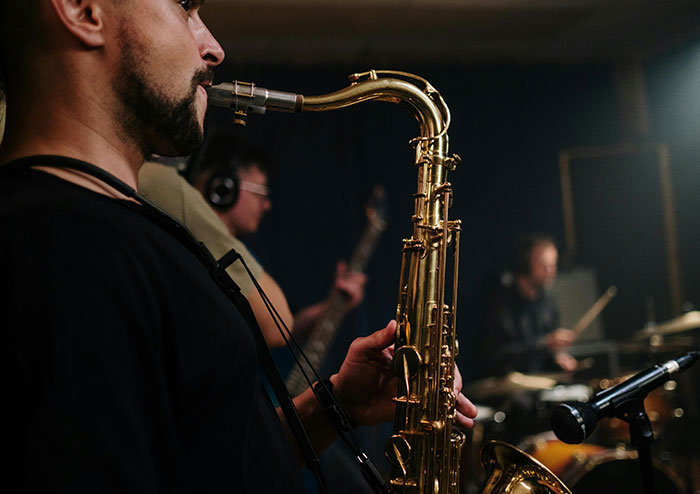 Man playing saxophone in a dimly lit room with band members, illustrating rich people behavior in exclusive settings.