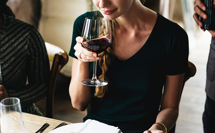 Woman in a black dress holding a glass of red wine, illustrating rich people behavior in high-end dining settings.