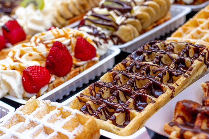 Assorted European-style waffles with strawberries, bananas, and chocolate drizzle on white trays, popular among European netizens.