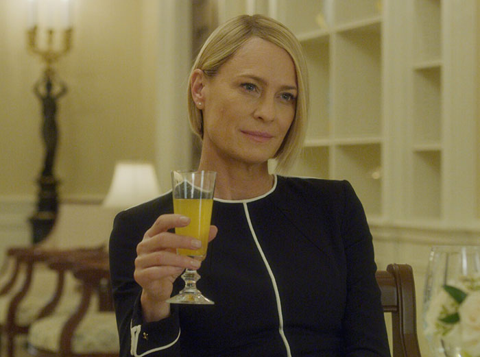 Woman in a black dress holding a glass of orange juice, with Kevin Spacey plastic surgery rumors trending online.