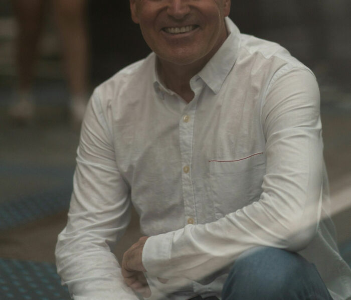 Smiling man in white shirt sitting casually, illustrating male coworkers sharing statements about women at work.