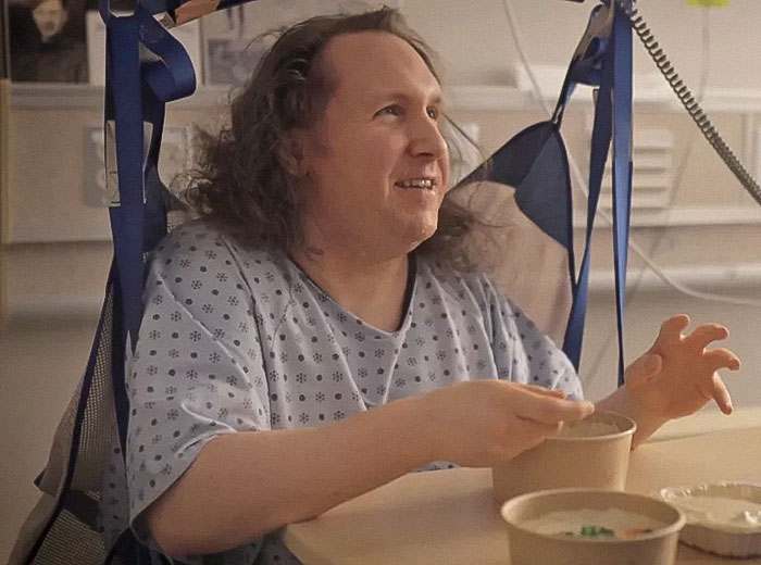 Man in hospital gown sitting and eating, highlighting issues of being trapped and mistreated by hospital staff.