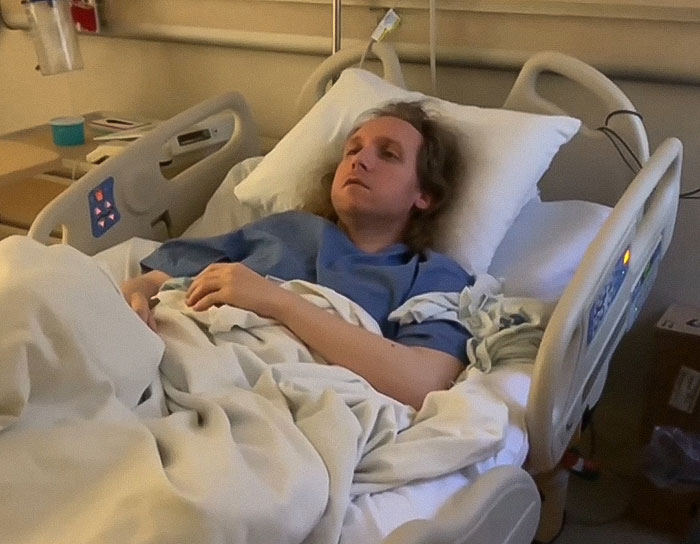 Man lying in hospital bed appearing distressed, highlighting man trapped in hospital for 9 years and exposing staff.