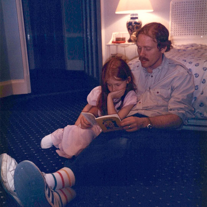 Ron Howard&rsquo;s nepo baby Bryce Dallas Howard as a child reading a book with a man in a cozy dimly lit room.