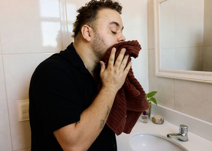 Man drying face with towel in bathroom symbolizing annoyance over roommate’s boyfriend using her shower. Man drying face with towel in bathroom symbolizing annoyance over roommate’s boyfriend using her shower.