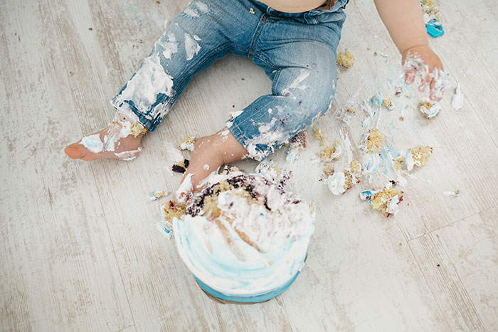 Toddler in jeans sitting on floor, covered in cake and frosting, illustrating messy kids creating household chaos. Toddler in jeans sitting on floor, covered in cake and frosting, illustrating messy kids creating household chaos.