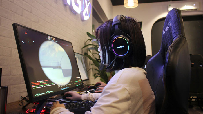 Woman wearing headphones gaming intensely on a desktop during a late-night gaming marathon at home.