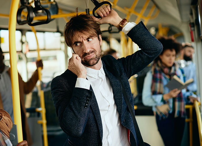 Man holding bus handle and talking on phone looking concerned about removing stuff while standing on crowded bus.