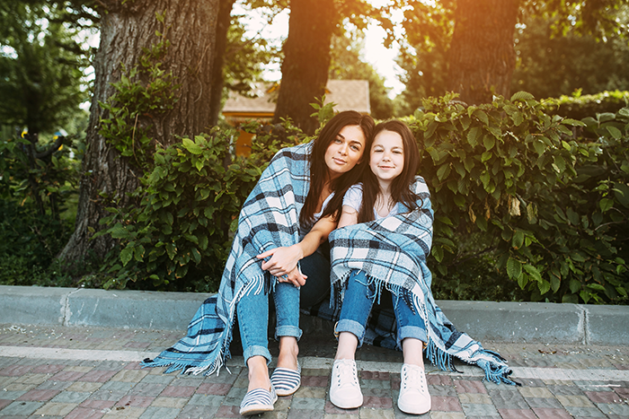 Teen niece and aunt wrapped in a blanket at the park, showing their close bond despite conflict during shopping trip cancellation.