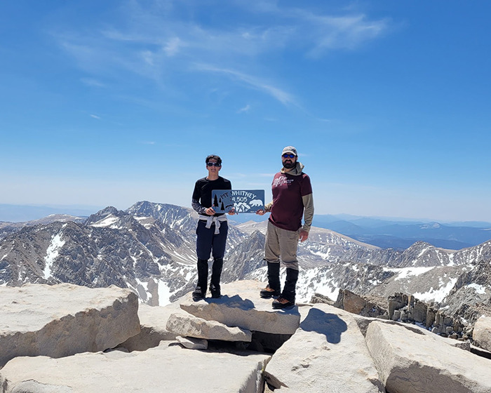 Two hikers on a snowy mountain peak holding a sign, illustrating the terrifying words of a hallucinating 14YO son.