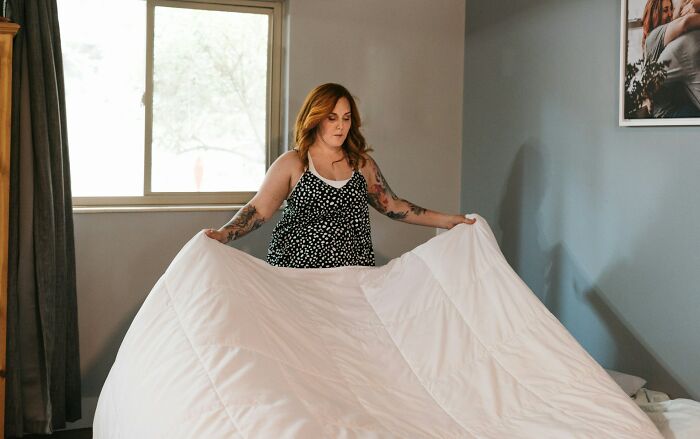 Woman making a bed in a bedroom, illustrating concepts related to pregnancy and having twins.