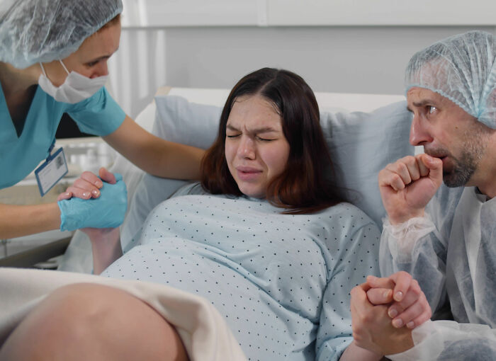 Pregnant woman in labor supported by partner and nurse, illustrating childbirth and postpartum facts in hospital setting.