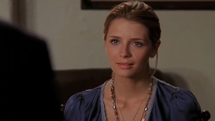Young woman in a blue blouse sitting indoors with a thoughtful expression, representing tragic losses in TV shows.