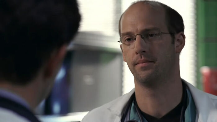 Doctor wearing glasses and a white coat speaking to a colleague, representing tragic losses in TV show history.