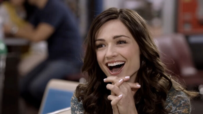 Young woman with curly brown hair smiling brightly in a casual setting, representing tragic losses in TV show history.