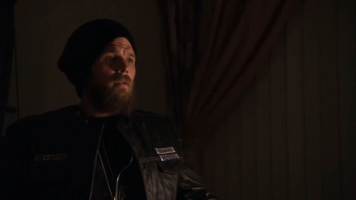 Bearded man in a dark leather jacket and beanie sitting in a dimly lit room, reflecting on tragic losses in TV shows.