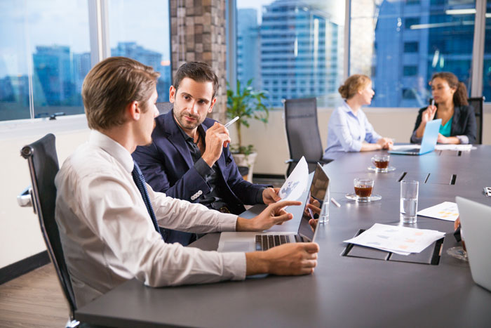 Two men discussing bug reports and exploratory testing in a modern office with city views and laptops on the table. Two men discussing bug reports and exploratory testing in a modern office with city views and laptops on the table.