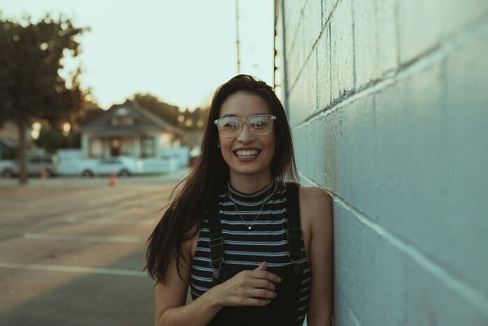 Young woman smiling and leaning against a wall, illustrating cultural no no in your country social behavior.