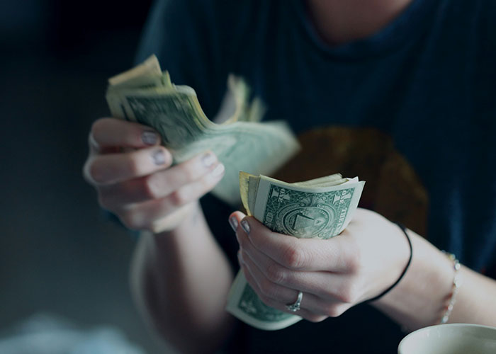 Person counting cash in hands, symbolizing money management and covering costs at a dry wedding event.