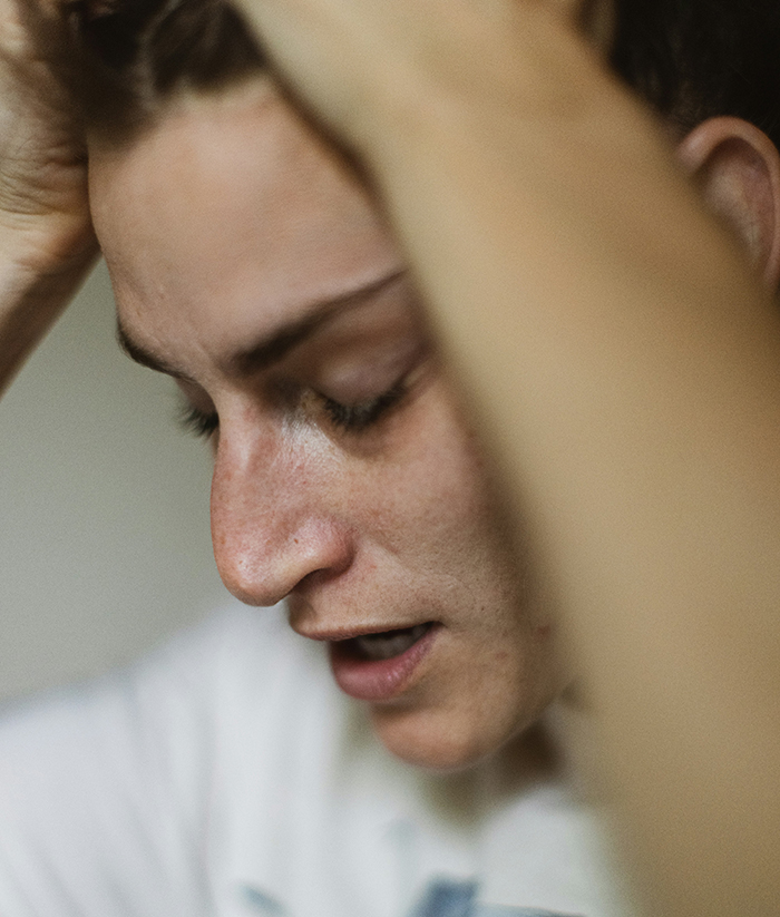 Young person holding their head in distress, experiencing intense guilt and emotional pain related to disturbing deathbed confessions.