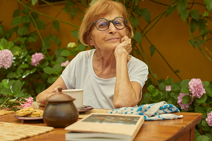Elderly woman sitting outdoors with tea and cookies, reflecting on disturbing deathbed confessions and guilt.