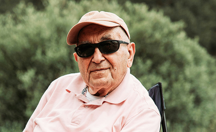 Elderly man in a pink shirt and cap wearing sunglasses outdoors, reflecting on disturbing deathbed confessions and guilt.