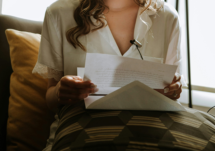 Person wearing a white shirt sitting on a couch, reading disturbing deathbed confessions on handwritten papers.