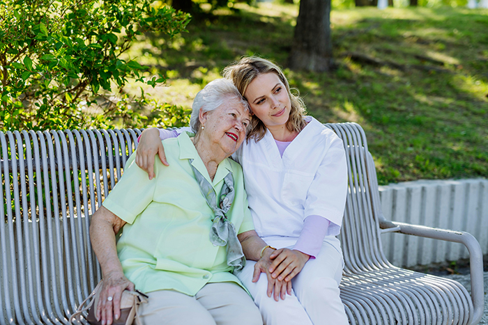 Elderly woman and caregiver sitting on a bench outdoors, sharing a comforting moment related to deathbed confessions.