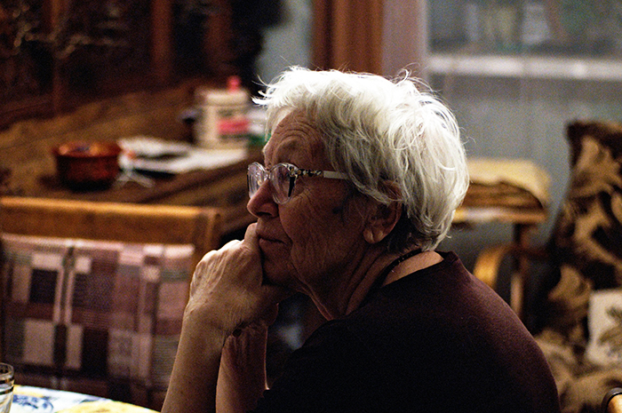Elderly woman with glasses sitting thoughtfully indoors, reflecting on disturbing deathbed confessions and guilt.